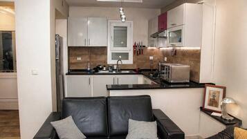 A modern kitchen with white cabinets, a black countertop, and a stainless steel refrigerator.
