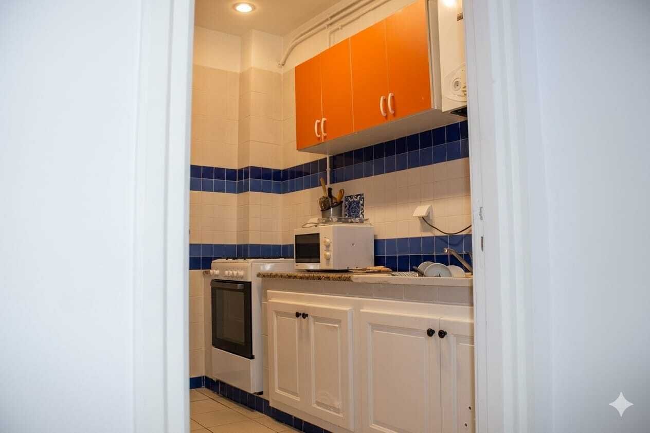 A kitchen with white cabinets, blue and orange tiles, a microwave, and a stove.