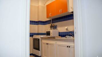 A kitchen with white cabinets, blue and orange tiles, a microwave, and a stove.