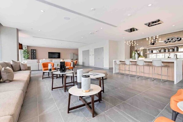 Uma sala de estar moderna com sofá, mesa de centro e cadeiras. Há uma área de cozinha com balcão e banquetas.