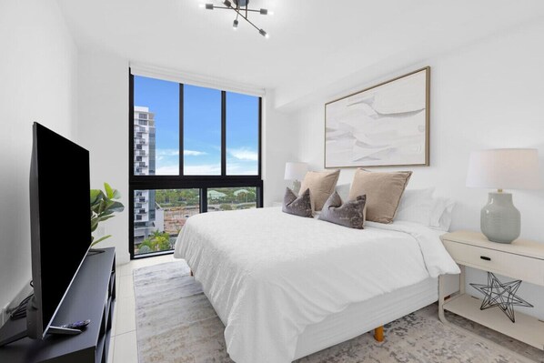 Une chambre moderne avec un grand lit, une télévision et une vue sur le paysage urbain, visible à travers une grande fenêtre.