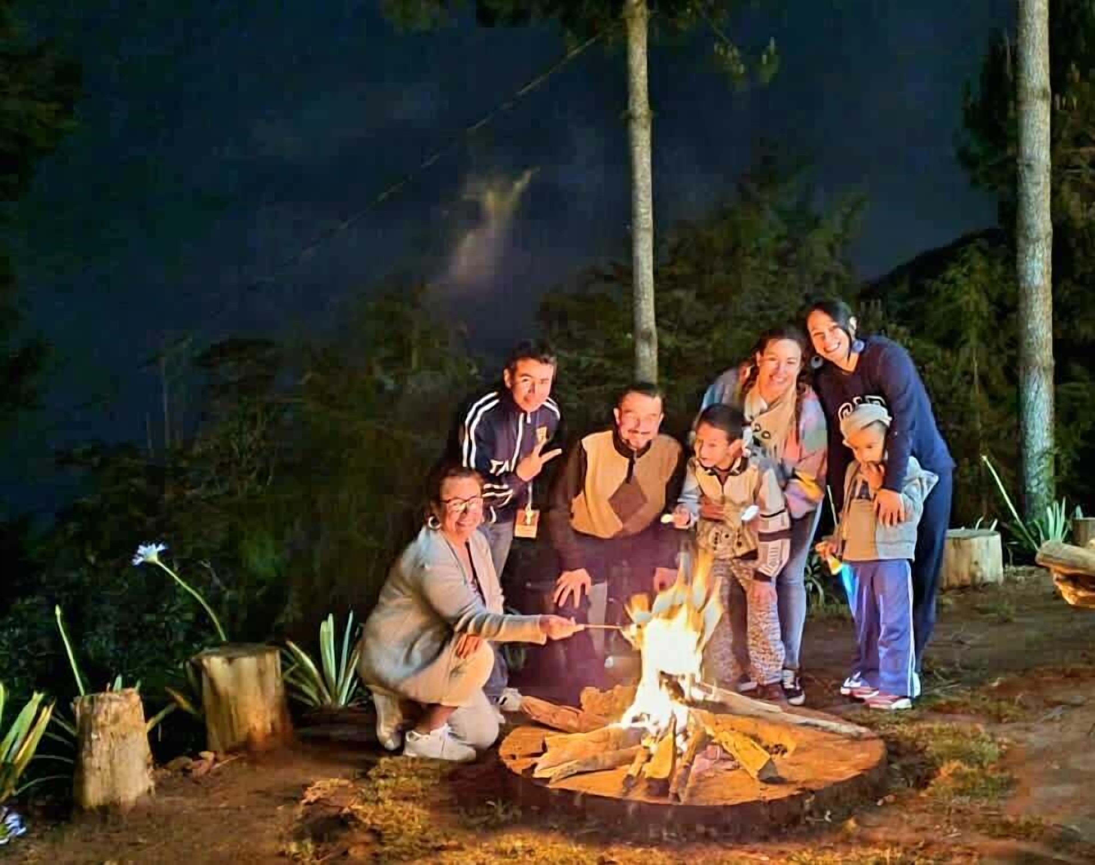 A group of people gathered around a campfire in a wooded area at night.