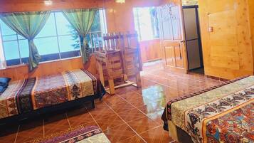 A room with four beds, each with a patterned bedspread, wooden walls, and a tiled floor.