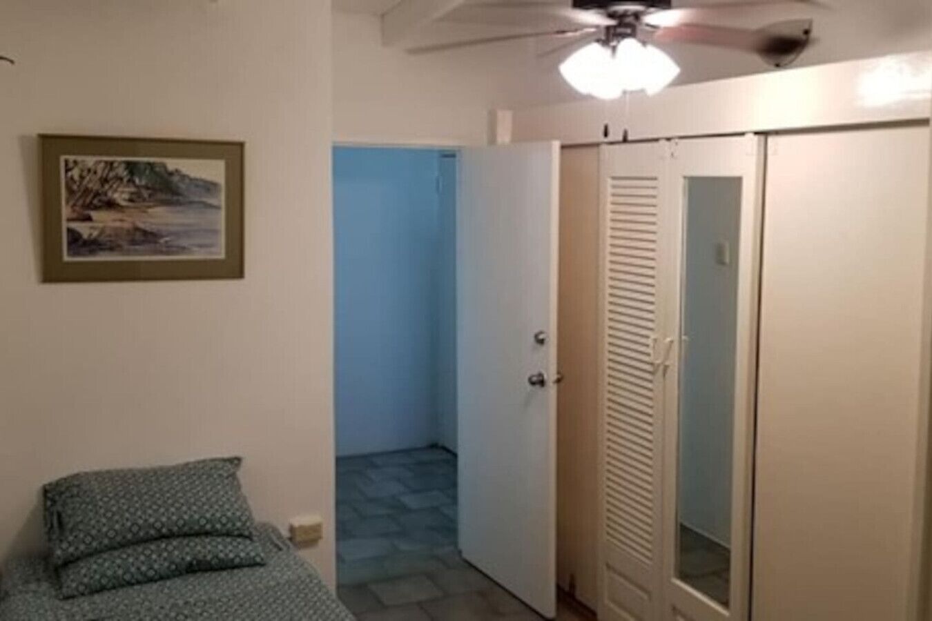 Ein Schlafzimmer mit Bett, Kleiderschrank, Deckenventilator und einer Tür zu einem anderen Raum.