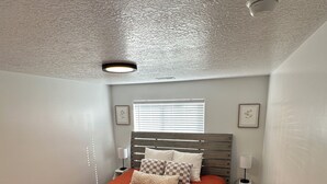 Une chambre à coucher avec un lit, une table de chevet, une lampe et un luminaire au plafond.