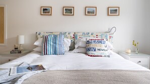 A neatly made bed with a striped pillow and a pillow with text, a bedside table with a lamp, and three framed pictures on the wall.