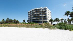 Un hôtel à plusieurs étages, doté de balcons, situé près d’une plage bordée de palmiers et de sable.