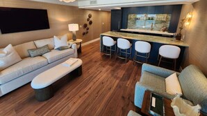 Un salon moderne avec un canapé, un pouf et un coin bar équipé de tabourets.