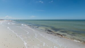 Une plage à l’eau claire, avec un rivage sablonneux et une jetée qui se dessine à l’horizon.