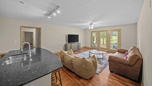 A modern living room with a kitchen area, a large bean bag, a brown sofa, and a flat-screen TV.
