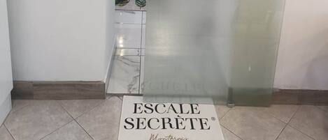 Een receptiezone met een deur van geëtst glas, een welkomstbord en een vloerteken met de tekst 'ESCALA SECRETÉ Montargues'.