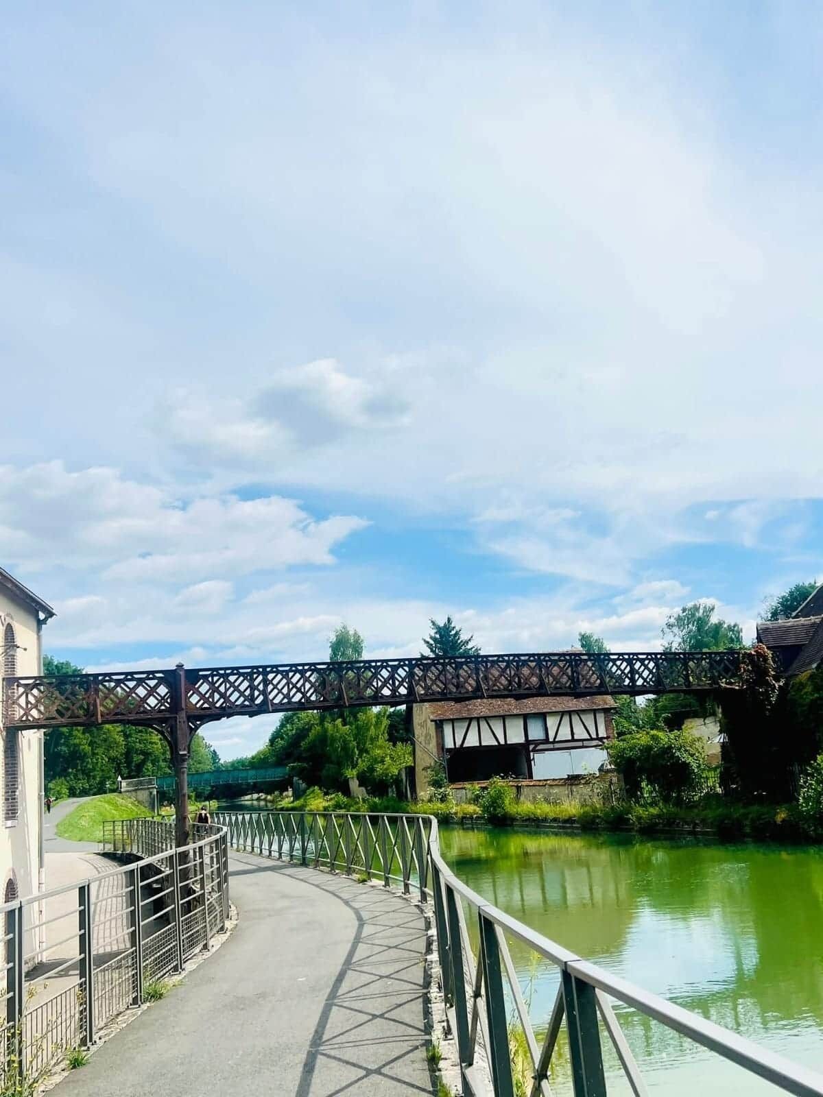 Un pont piétonnier enjambant une rivière, doté d’une rambarde métallique et d’un chemin piétonnier.