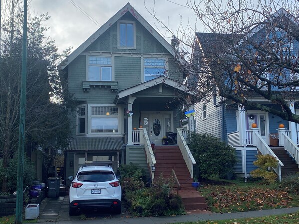 Uma casa de dois andares com garagem, um carro estacionado em frente e uma escadaria que leva à porta da frente.