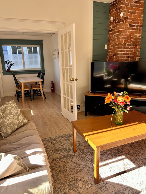 Una sala de estar con un sofá, una mesa de centro con un florero, un televisor y una chimenea de ladrillo.