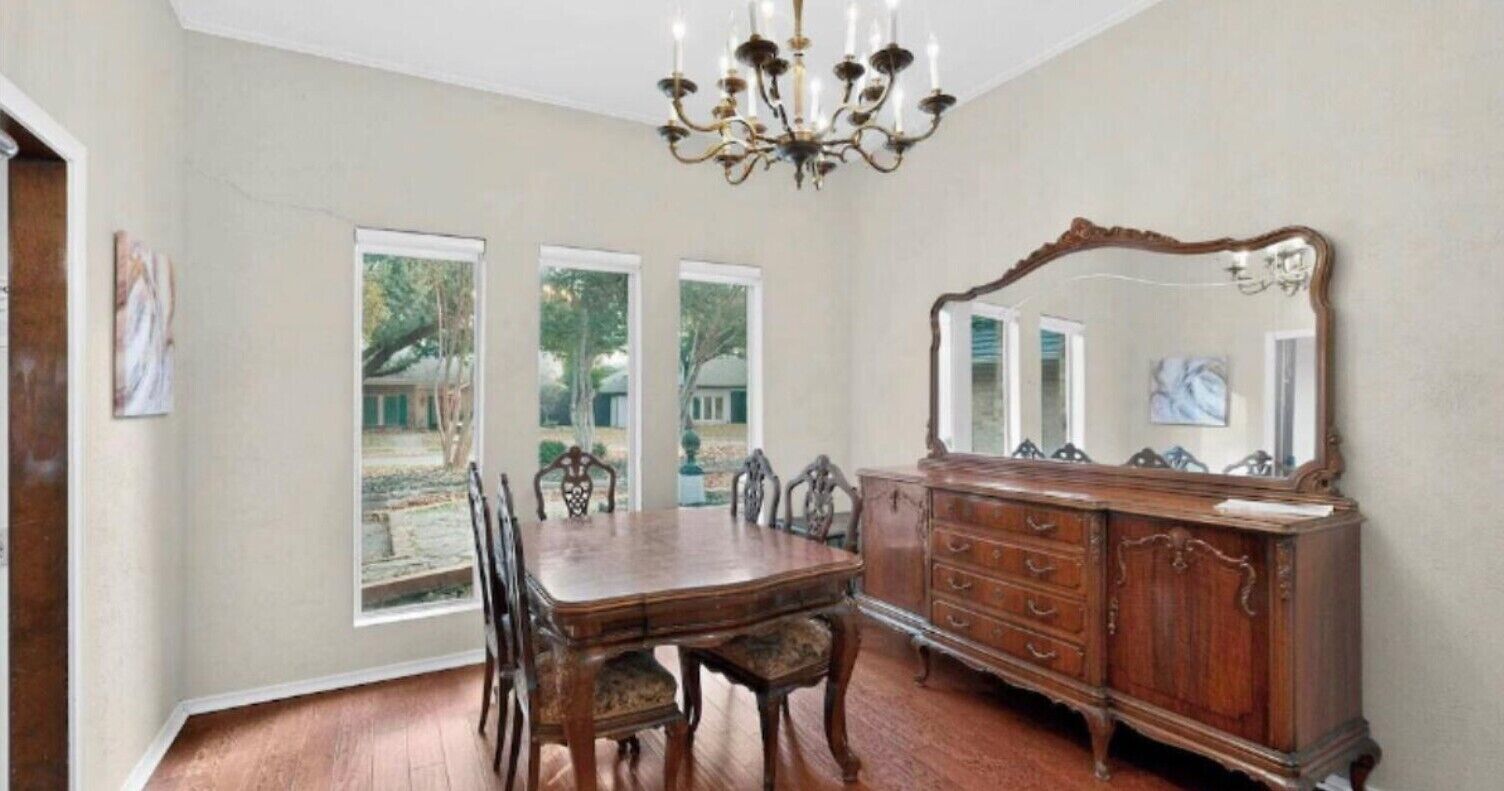 Ein Esszimmer mit Holztisch und -stühlen, einer Chandelierleuchtre, einem großen Spiegel und Blick durch die Fenster.