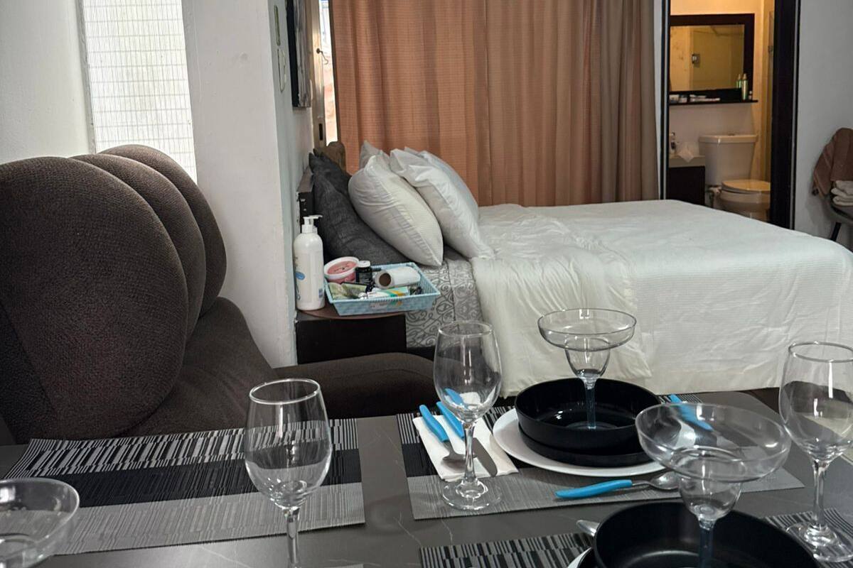 A hotel room with a neatly made bed, a dining table set for two, and a window with blinds.