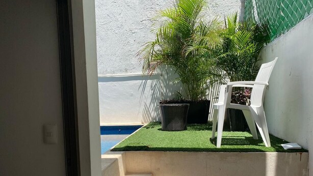 Pequeño espacio al aire libre con una silla de plástico blanca, una planta en maceta y una escalera de concreto que lleva a una piscina.