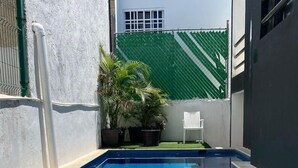 Ein rechteckiger Pool mit blauen Fliesen, umgeben von einer weißen Mauer und einem grünen Zaun.