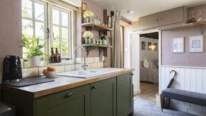 A kitchen with a wooden countertop, green cabinets, a sink, and a window with plants. - The Rabbit Hole | Cotswold Holiday Let | 1 Bed & Sleeps 2 (Langford, Lechlade)