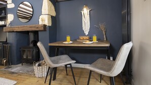 A dining area with a dark blue wall, a wooden table, two grey chairs, and a rustic decor including a stone wall and a hanging light fixture. - The Rabbit Hole | Cotswold Holiday Let | 1 Bed & Sleeps 2 (Langford, Lechlade)