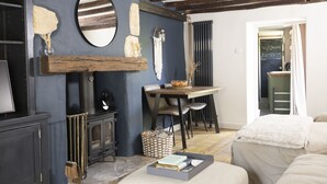 A cozy room with a fireplace, a dining table with chairs, and a bed. - The Rabbit Hole | Cotswold Holiday Let | 1 Bed & Sleeps 2 (Langford, Lechlade)