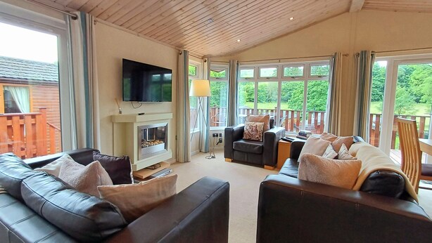 Ein großzügiges Wohnzimmer mit Kamin, Ledersofas, einem Flachbildfernseher und großen Fenstern mit Blick ins Freie.
