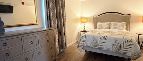 Une chambre à coucher avec un lit, une commode, un miroir et une fenêtre avec des rideaux.