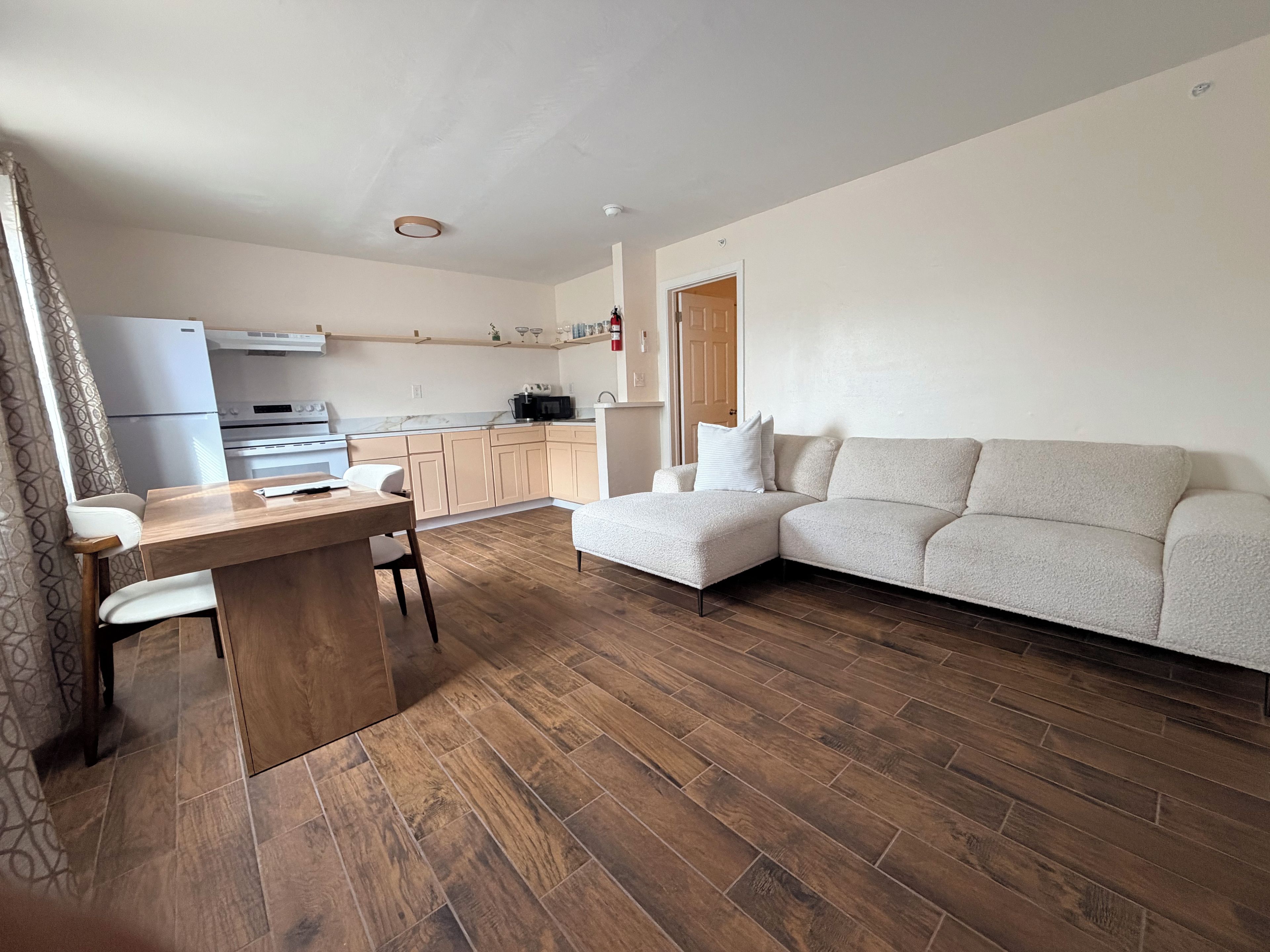 Ein modernes Wohnzimmer mit einem Holzesstisch, einer Couch und einer Küchenzeile im Hintergrund.