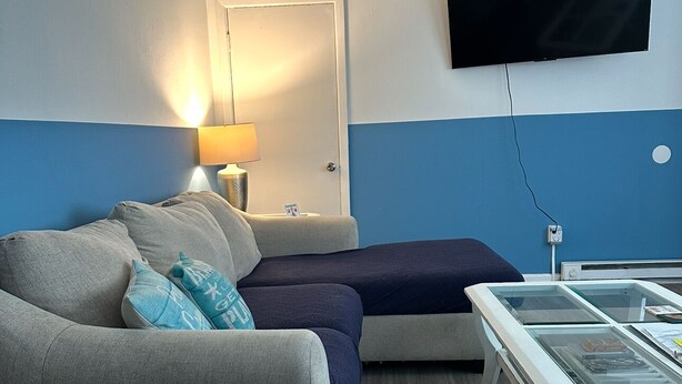 A modern living room with a grey sofa, a blue accent wall, a flat-screen TV mounted on the wall, and a glass coffee table.