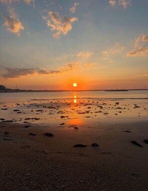 A beach with a sunset, calm water, and footprints in the sand.