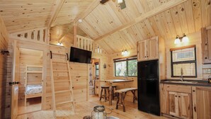 A wooden cabin interior with a bunk bed, kitchen area, and a dining table.