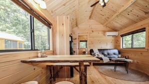 A wooden cabin interior with a dining table, stools, a sofa, and a fireplace.
