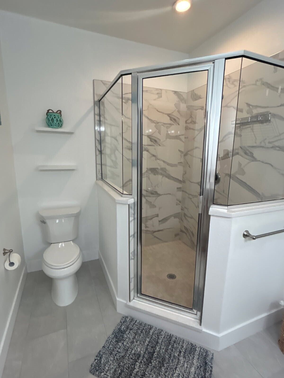 A modern bathroom with a glass-enclosed shower, a toilet, and marble walls.