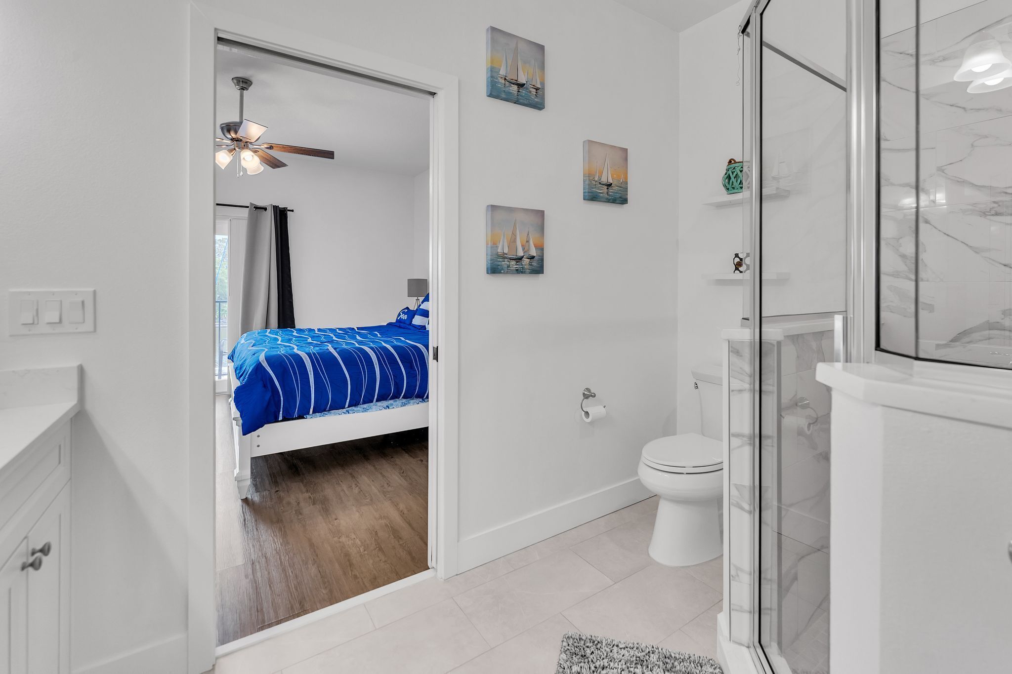 Een moderne badkamer met een douchecabine van glas, een toilet en een bed met een blauw gestreept beddegoed.