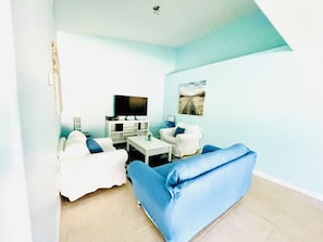 A living room with a white sofa, a blue sofa, a coffee table, a flat-screen TV, and a painting on the wall.