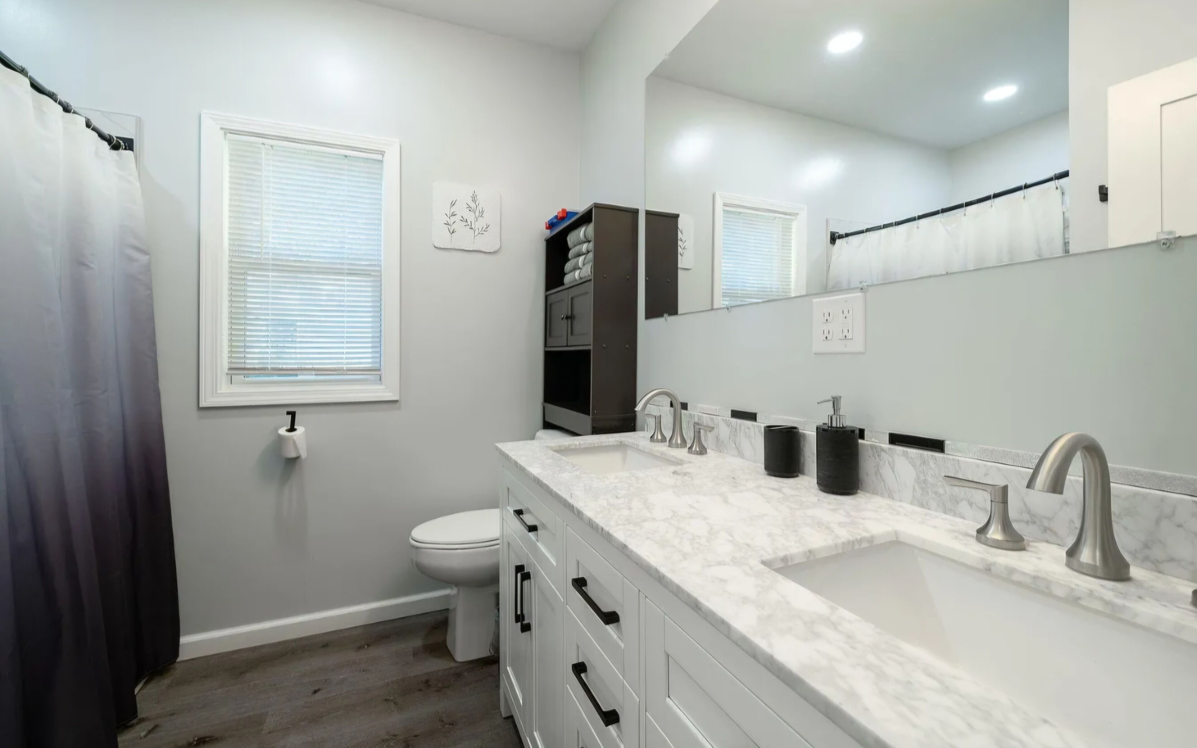 Une salle de bain moderne avec un lavabo blanc, deux robinets, des toilettes et un rideau de douche.