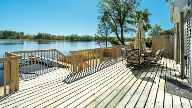 A wooden deck with a view of a lake, outdoor furniture, and a wooden fence.