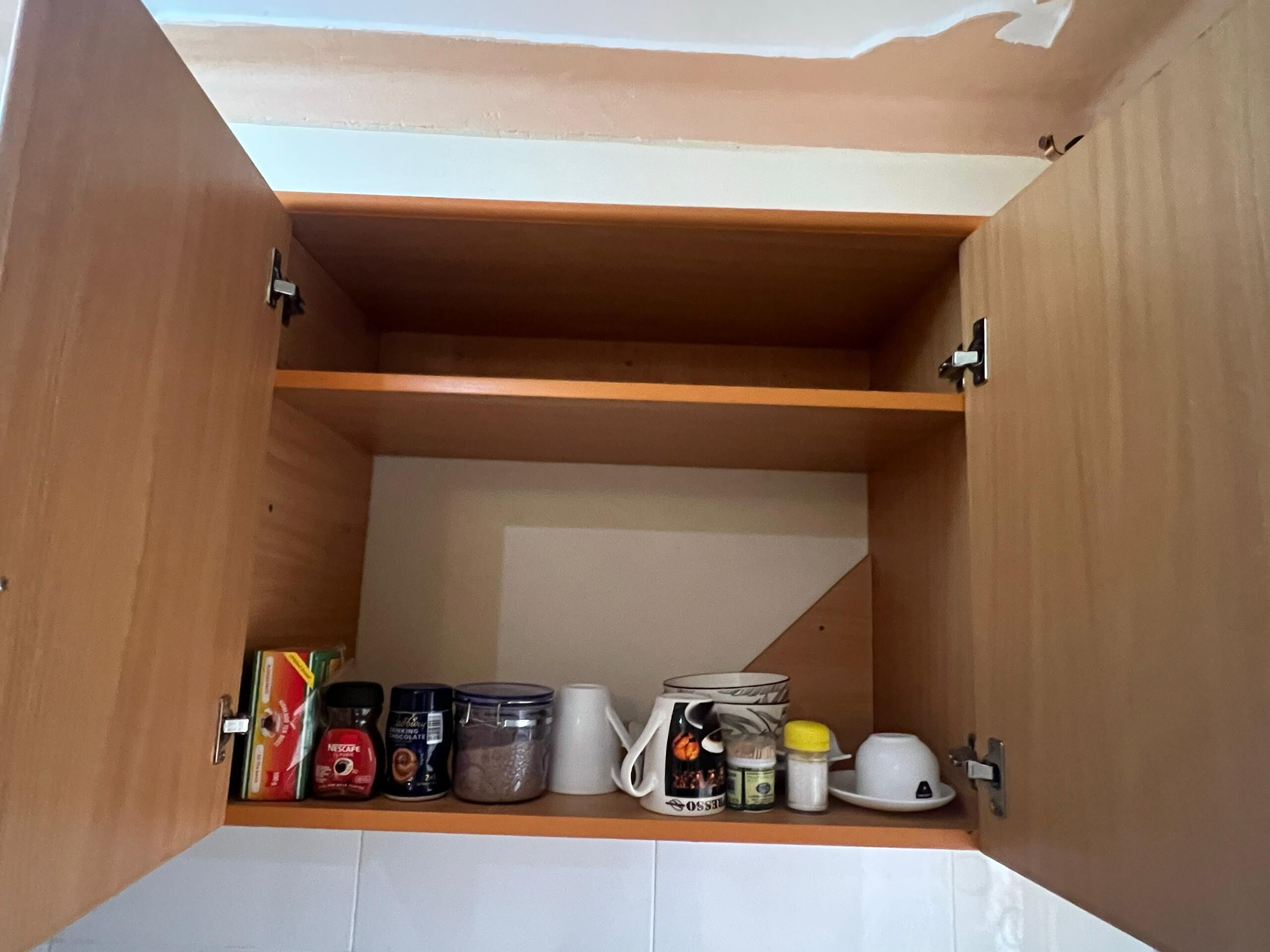 A wooden cabinet with shelves containing various items like a coffee maker, a mug, and containers.