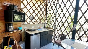 Eine kompakte Küche mit Mikrowelle, Kaffeemaschine und einem kleinen Kühlschrank. Ein Esstisch mit Stühlen und ein Korbwicker-Korb mit Snacks sind vorhanden.