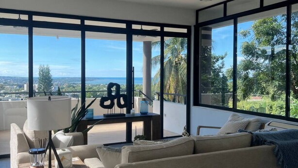 Uma sala de estar moderna com uma janela grande, um sofá, uma mesa de centro e um abajur.