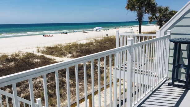 A beach view from a balcony with a white railing, sandy beach, and ocean.