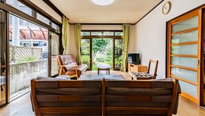 Una sala de estar moderna con un sofá, sillas, una mesita de centro y un televisor. Amplias ventanas ofrecen vistas al exterior.