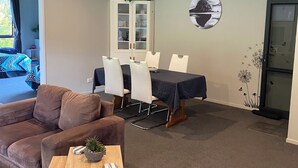 Un salon avec un canapé marron, une table basse en bois et un coin repas comprenant une table et des chaises. On y trouve également un meuble avec des portes en verre et un tableau accroché au mur.