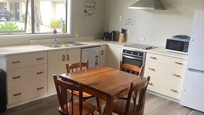 Une cuisine compacte avec une table à manger en bois, des placards blancs, un four encastré et un four à micro-ondes.