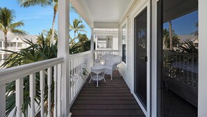 Un balcon abrité avec des balustrades blanches, une chaise en osier blanche et une petite table.