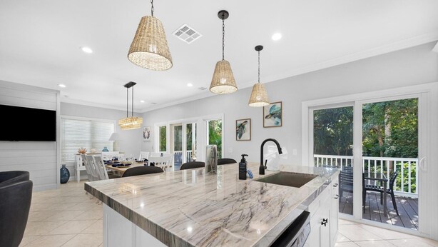 Une cuisine moderne dotée d’un grand îlot central, de luminaires suspendus et donnant sur une terrasse extérieure.