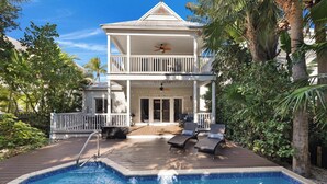 Une maison à deux étages avec une piscine, un balcon doté d’un ventilateur de plafond et une terrasse avec des chaises longues.