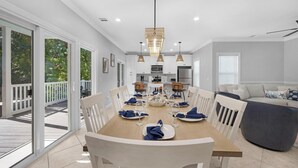 Un coin repas avec une grande table en bois dressée pour six personnes, des chaises blanches et un lustre.