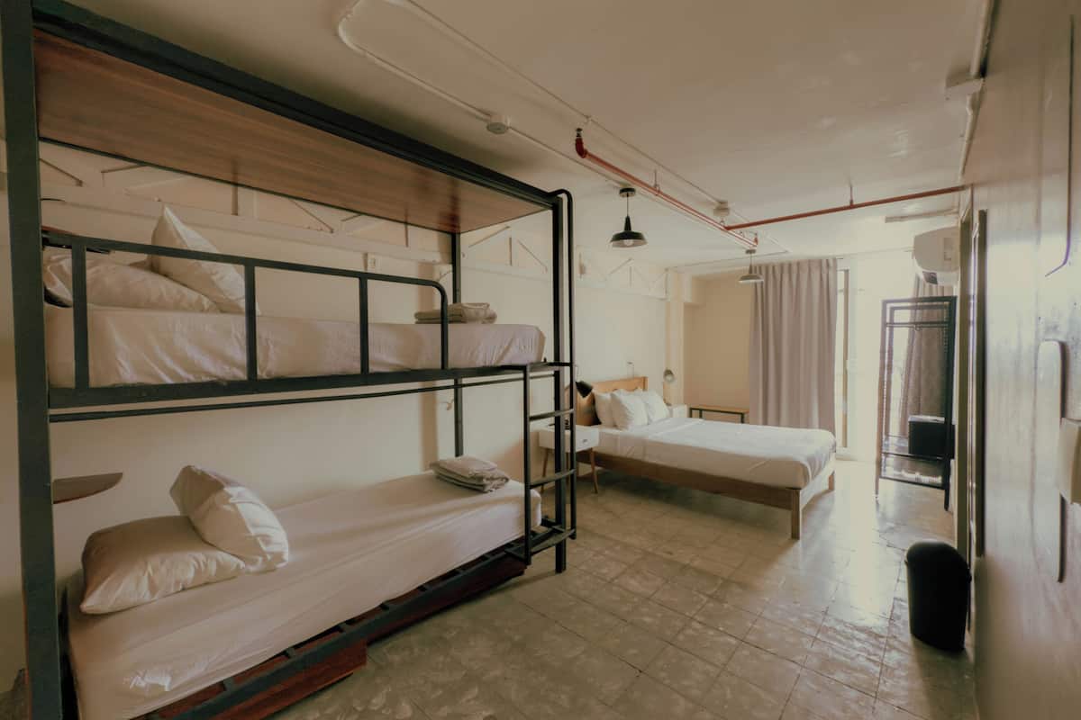 Um quarto de dormitório com beliches, uma escrivaninha, uma cadeira e um pequeno cesto de lixo.