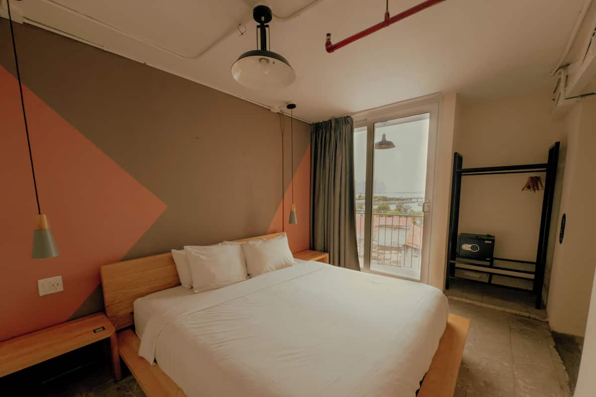 Quarto com cama, mesa de cabeceira, guarda-roupa e vista para o exterior.